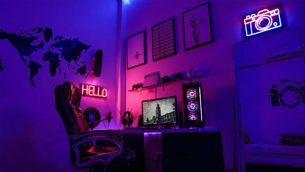 A gaming workspace with a computer, neon signs, and wall art in purple light