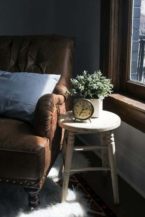 Brown leather padded sofa armchair next to white wooden stool chair with round gray metal analog clock