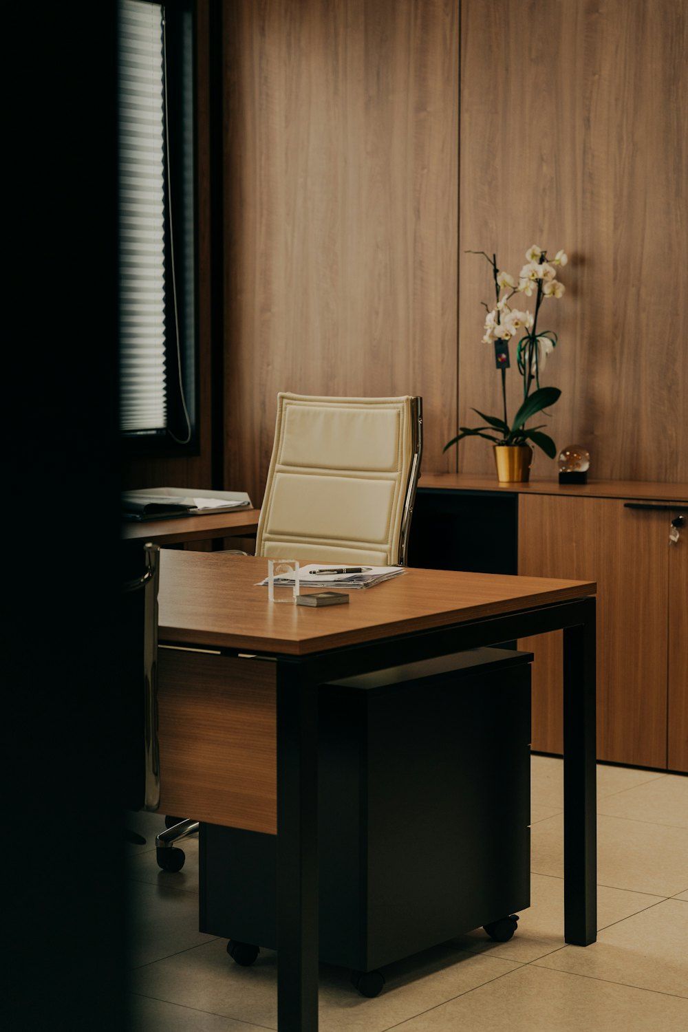 A desk with a chair and a vase of flowers