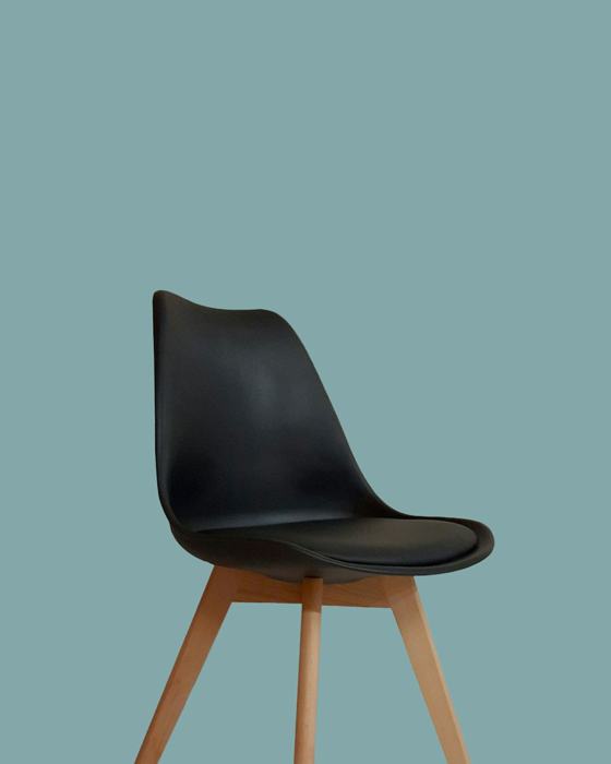 A black molded chair with wooden legs against a solid teal background