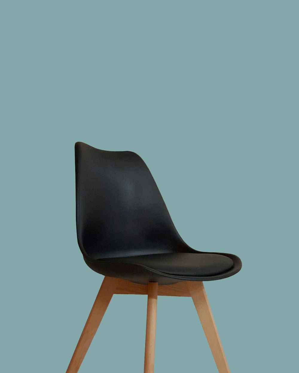 A black molded chair with wooden legs against a solid teal background
