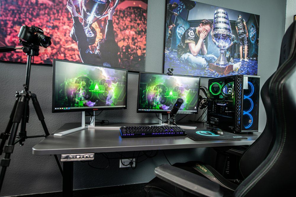 A gaming desk with two monitors, a computer tower, and a camera on a tripod