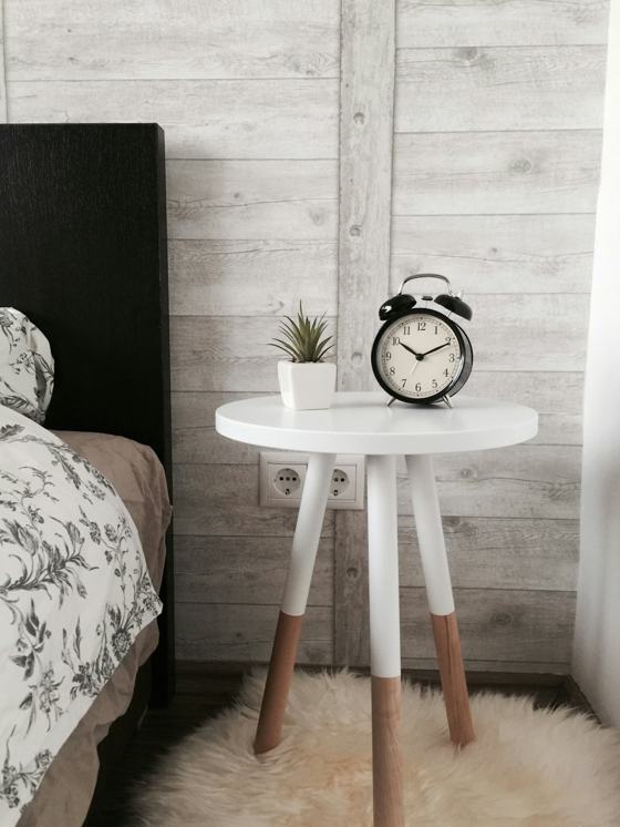 Black alarm clock at 10:10 on white wooden table near table