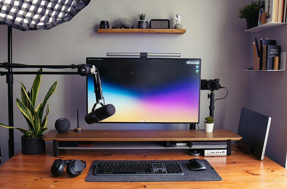 A desk with a monitor, keyboard and headphones