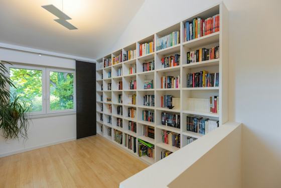 A large white bookshelf filled with many books in a bright home office