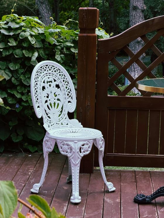 A white ornate metal chair on a wooden deck beside a lattice fence