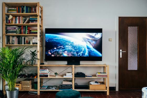 Black flat screen tv turned on near brown wooden shelf