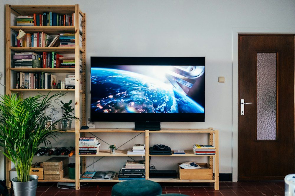 Black flat screen tv turned on near brown wooden shelf