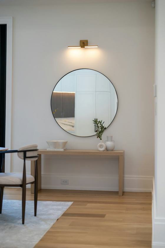 A round mirror above a wooden console table with decor